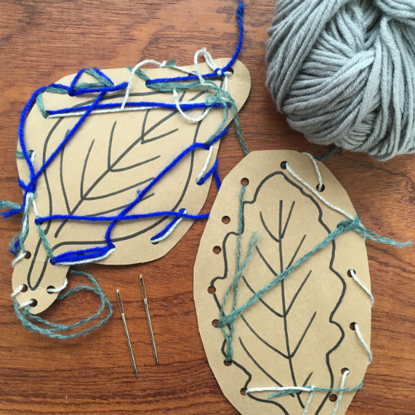 children's threading project with holes punched into cardboard leaf shapes threaded with wool